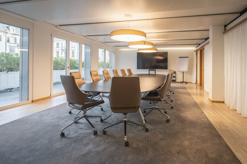 Meeting room with large oval table, leather chairs, large glass windows with city view, monitor