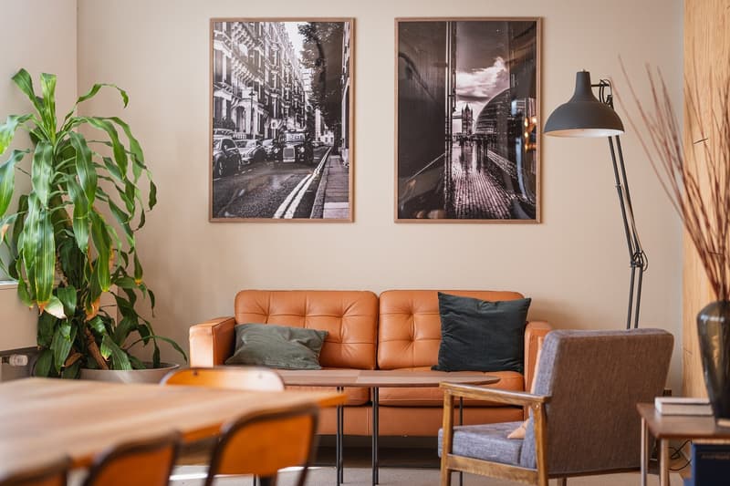 interior of a living room, leather couch, coffee table, framed art, plant, wooden floor, table, wooden chairs, lamp, wooden cabinet, books, side table