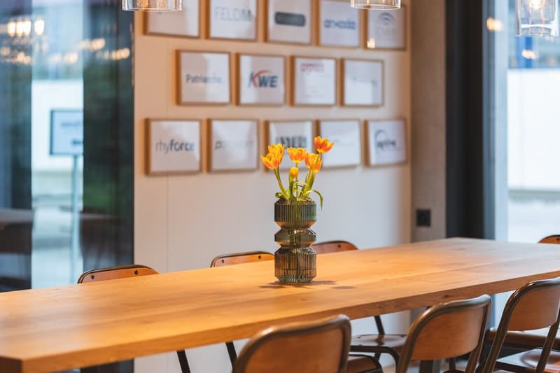 Wooden table with flowers in a glass vase, brown chairs, light wall with framed pictures