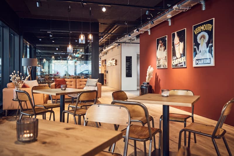 Wooden tables, metal chairs, round candles, couch, beige walls, glass windows, vintage posters, hanging lights, metal pipe