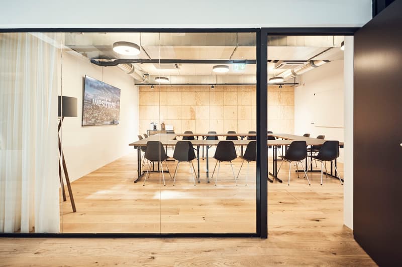 Glass walls, wooden floor, tables and chairs arranged in rows, white curtains, lamp, coffee maker, artwork on wall