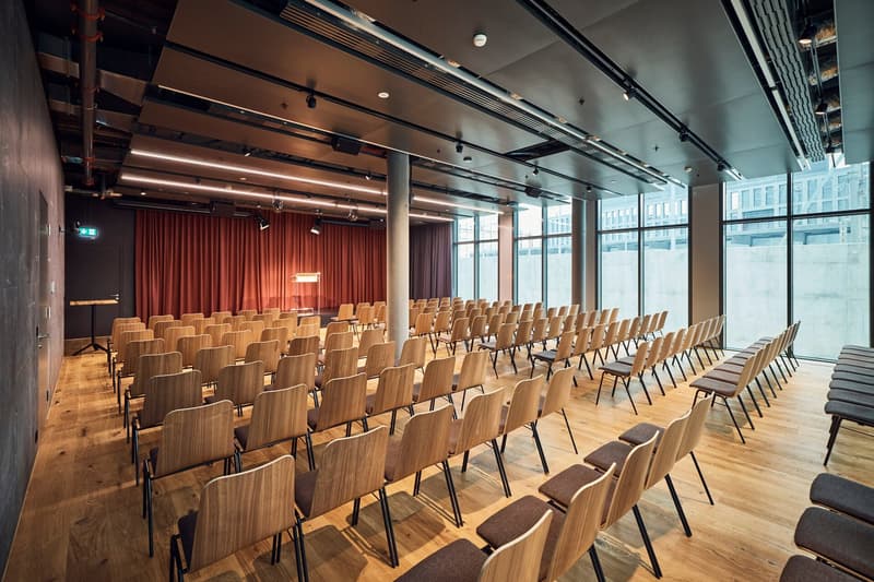 wooden floor, stage with curtains, rows of chairs, large windows