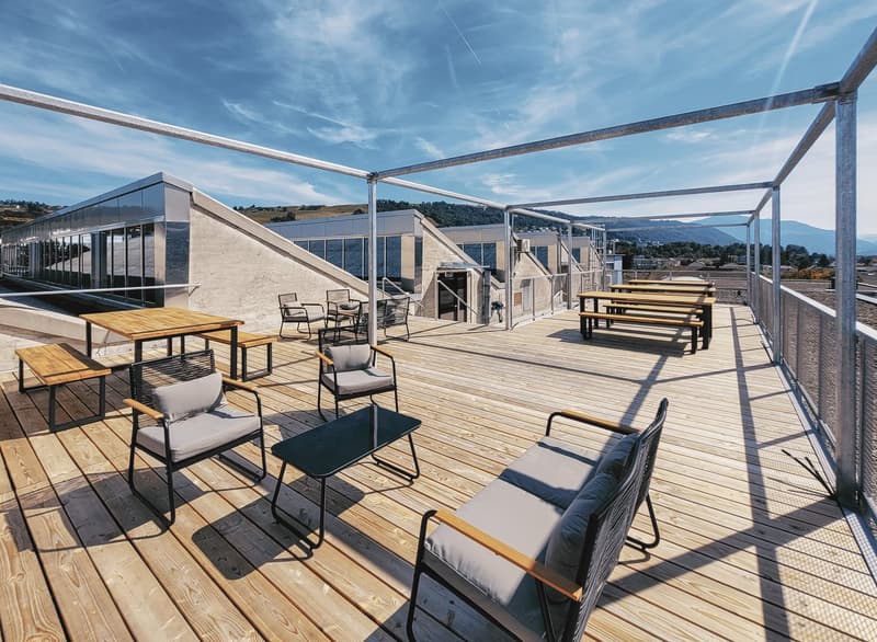 Wooden floor terrace with glass railings, modern seating, round tables, distant mountains and sky in the background