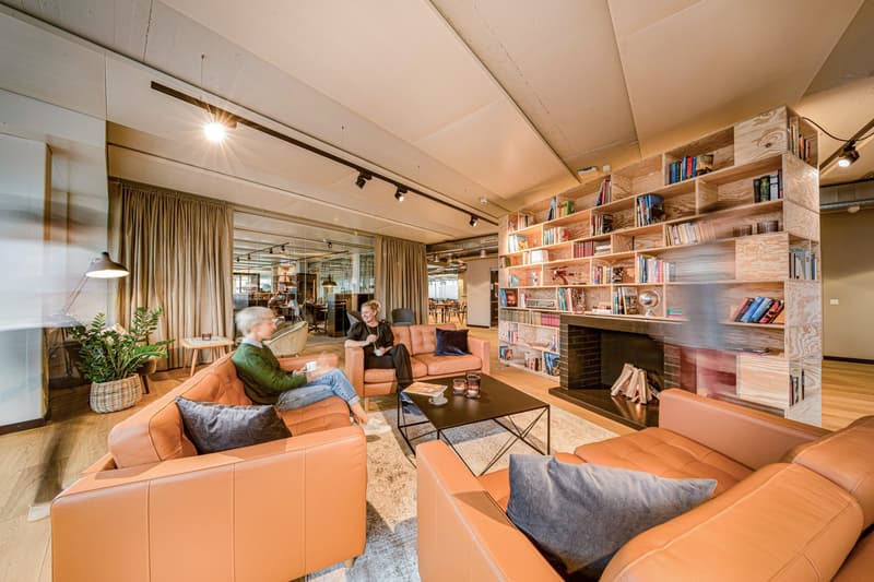 Two people sitting on leather sofas, glass coffee table, potted plant, fireplace, bookcases, wooden floor
