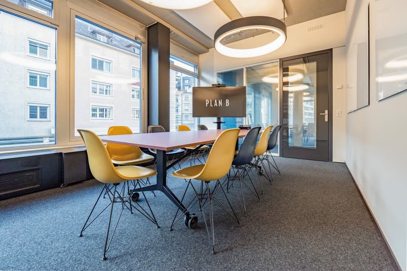 empty meeting room with yellow chairs, long rectangular table, monitor, windows, double doors