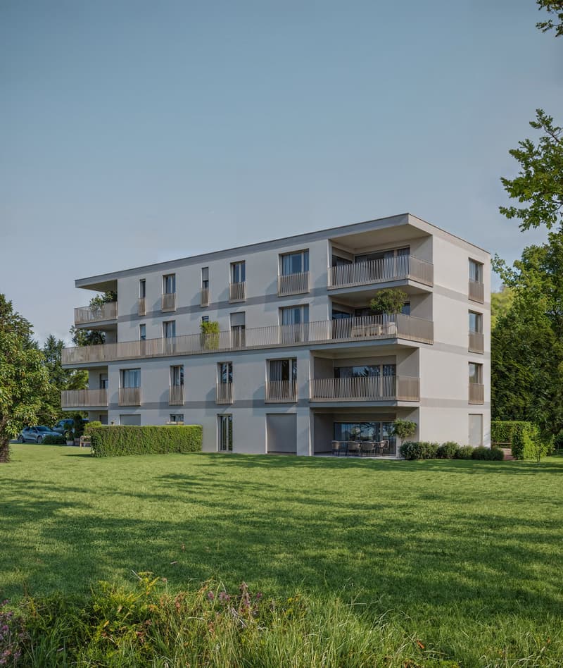 4-story apartment building with balconies, surrounded by a grassy lawn and trees