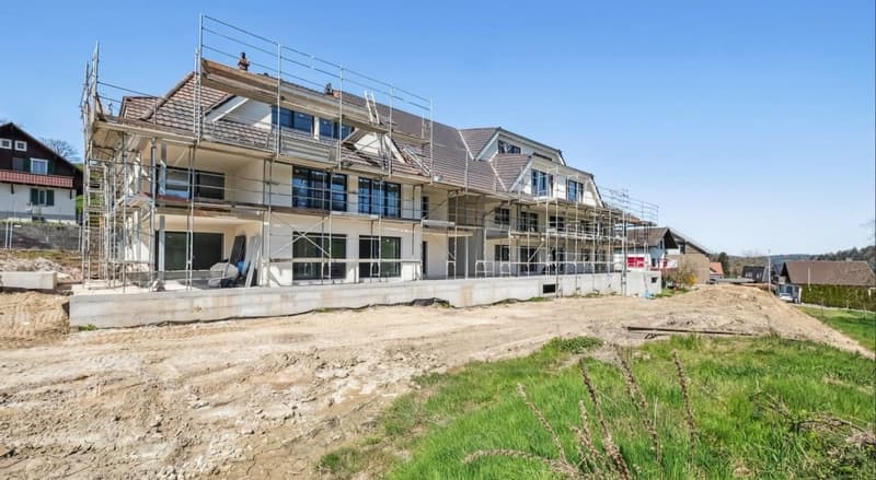 House under construction with scaffolding, tile roof, multiple windows, surrounded by dirt and grass