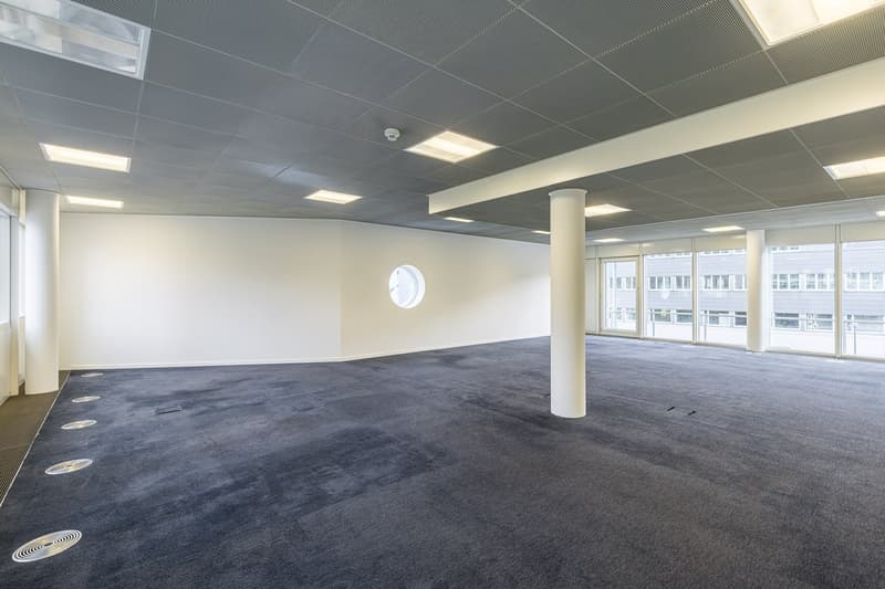 empty office space, white walls, ceiling with recessed lighting, two pillars, circular window on wall, large windows
