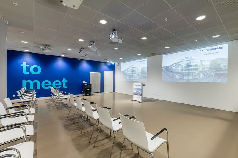 Empty meeting room with white chairs, blue wall, projector screens, podium, radiator
