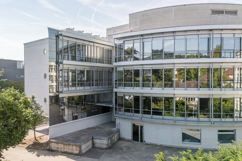 modern building, curved facade, glass windows, steel and glass balconies, parking area