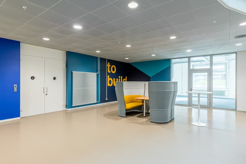 Empty room with blue walls, white door, yellow and gray seating, white table, silver railing, large windows, radiator