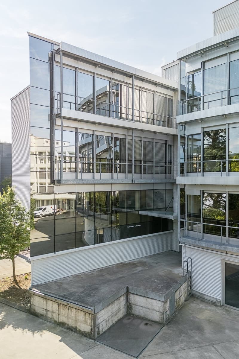 Multi-story commercial or office building with glass facade, balconies, and a raised ground floor entrance.