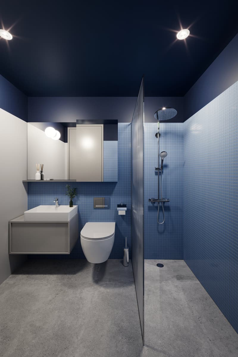 Modern bathroom with blue tiled walls and a walk-in shower with overhead showerhead. The room includes a white toilet, a white pedestal sink with silver faucet, a mirror, and a silver toilet brush. The ceiling has recessed lights.