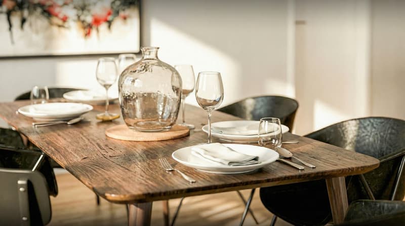 Dining room with wooden table, 6 chairs, plates, wine glasses, cutlery, and a glass vase