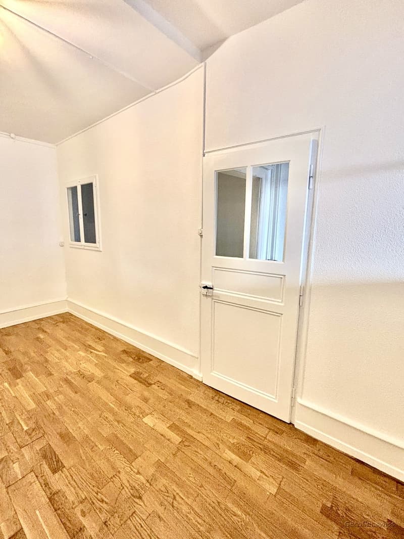 empty room with hardwood floors, white walls, small window, closed door, light fixture