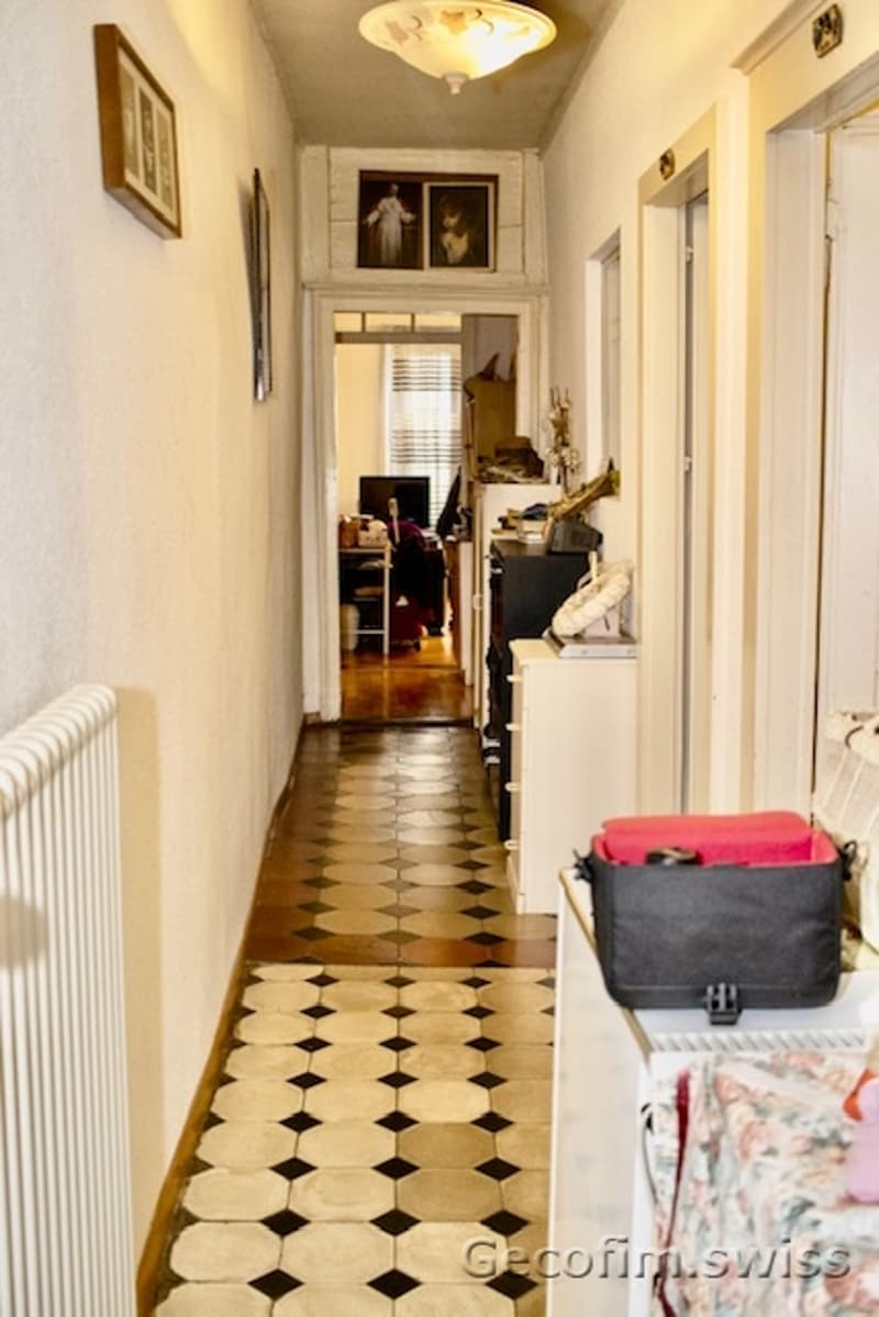 white walls, tiles on the floor, picture frame on the wall, black and white tile, cabinets on the side, radiator, photo frames on the wall, light fixtures on the ceiling