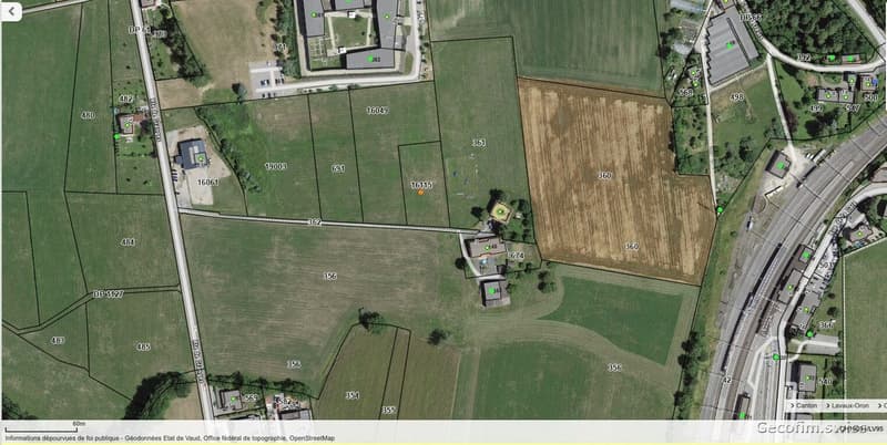 An aerial view of a wide, mostly green field with several plots and structures scattered throughout. Numbers and measurements are indicated on the image.