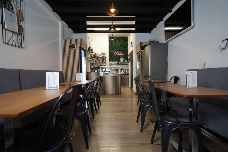 An empty dining room in a cafe with wooden tables and black chairs, wooden floors, wooden counters, refrigerators, and decorative wall art.