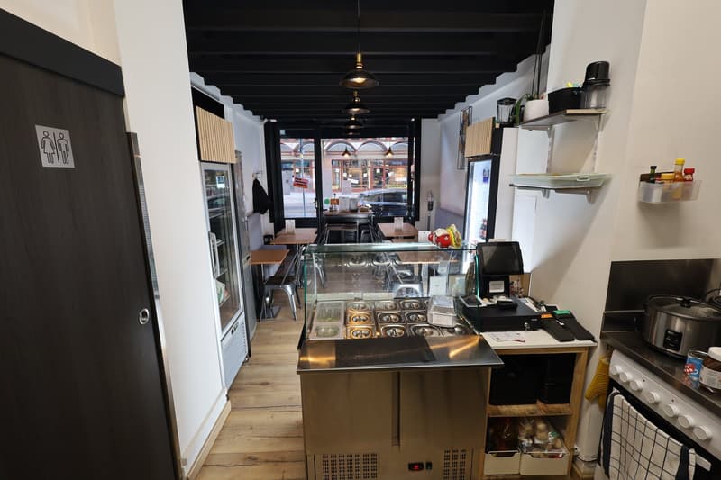 a kitchen with a display counter, refrigerators, shelves, and cooking appliances.