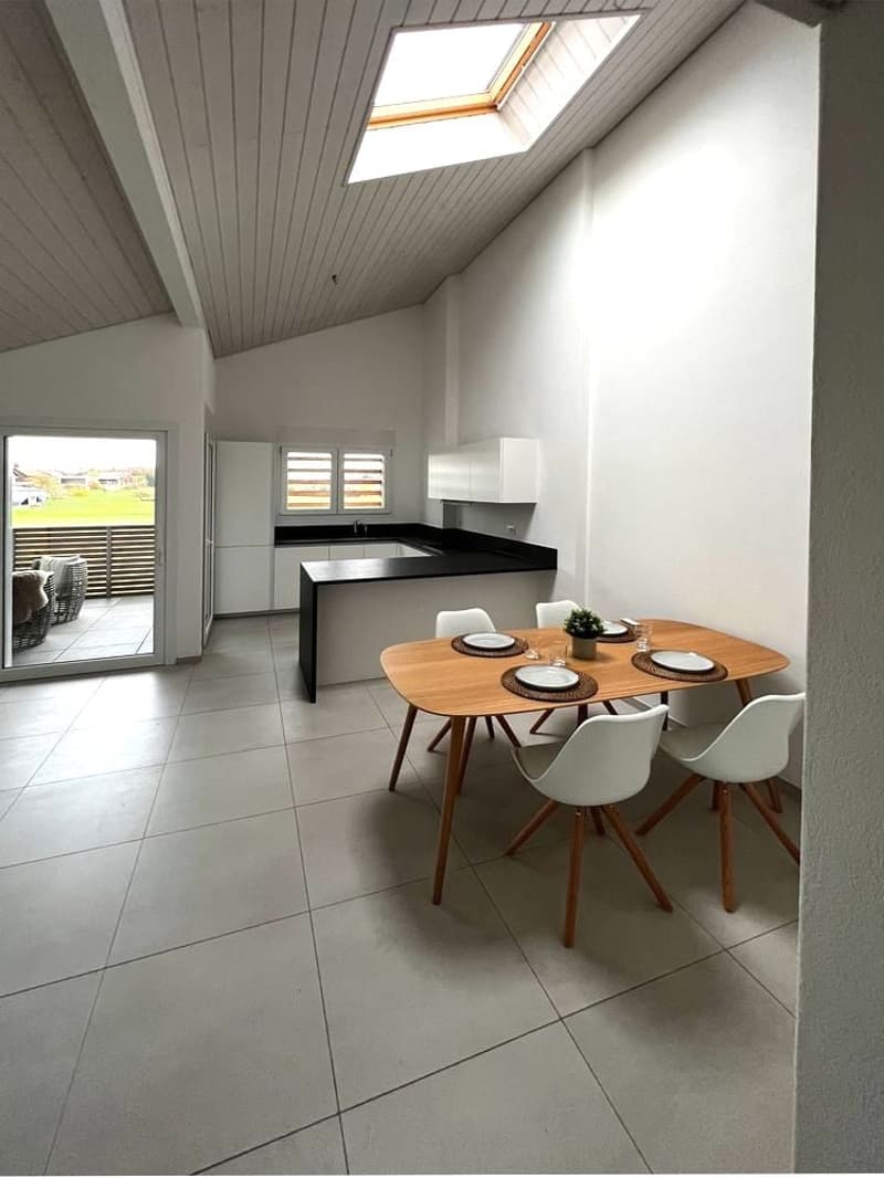 open-plan living area with kitchen, dining table with chairs, tiled floor, white walls, glass sliding door to balcony, skylight