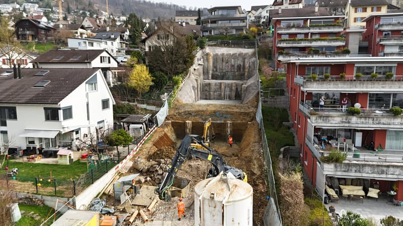Excavation area with construction equipment, buildings under construction, workers on site