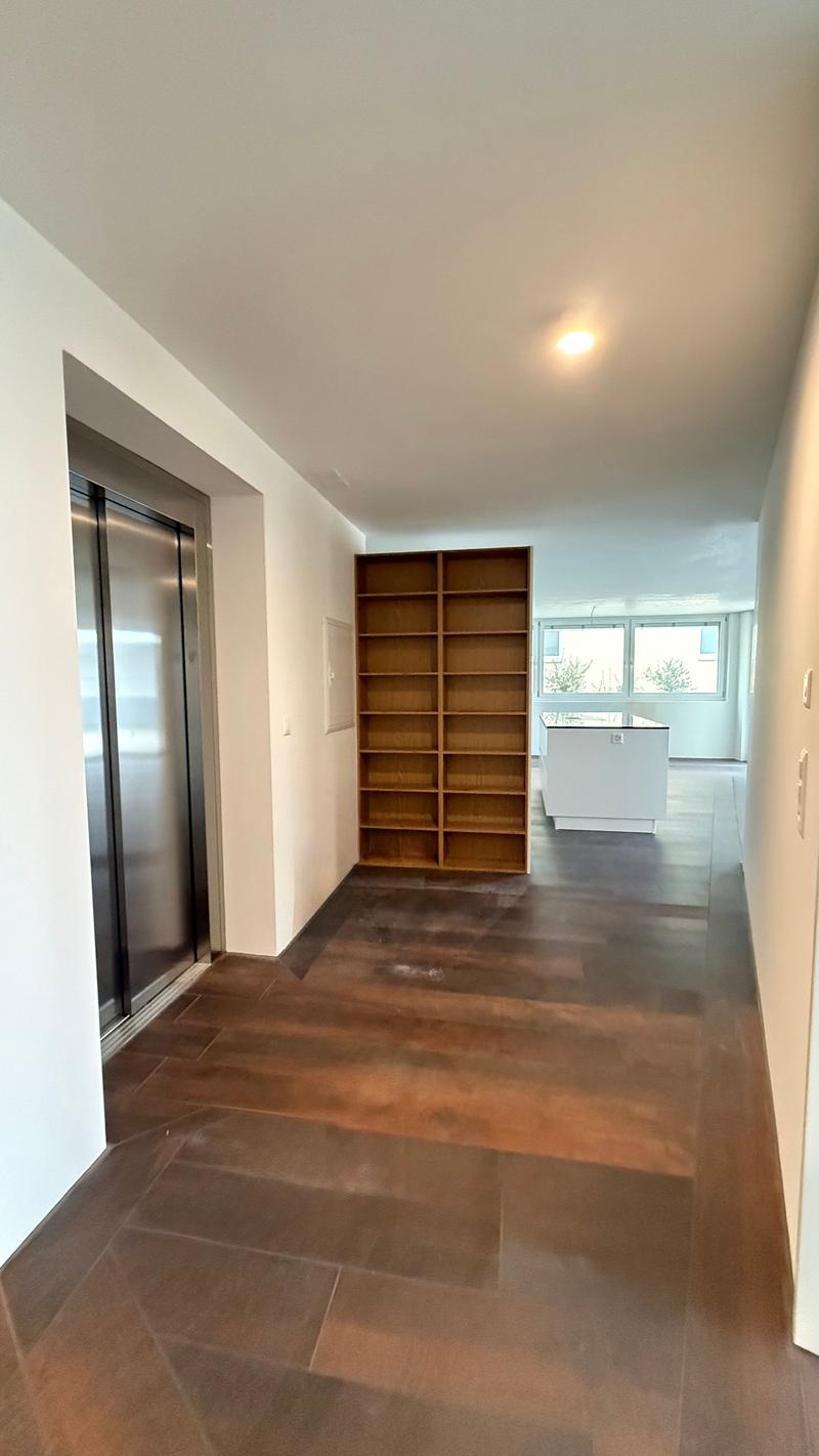 Living room with open shelves, kitchen area, elevator, wooden floor, windows