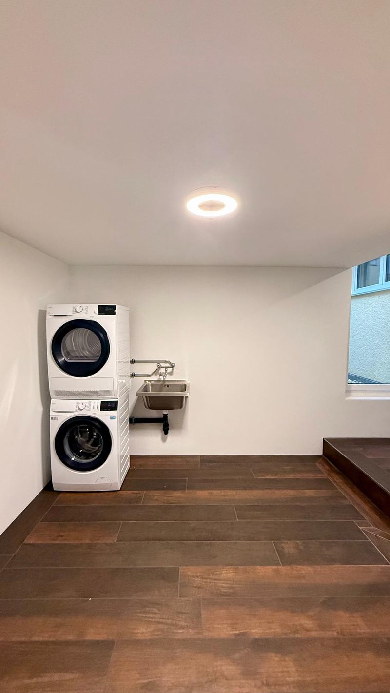 Laundry room with two stacked washer and dryer, sink, hard wood floor, white wall