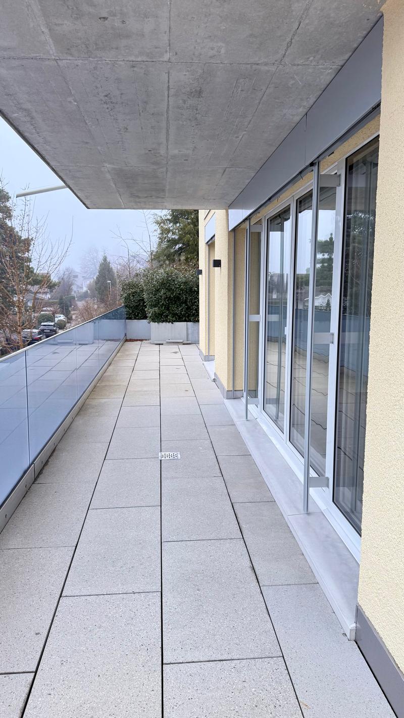 Large terrace with a paved floor, transparent glass railings, and an opening leading to the interior space.
