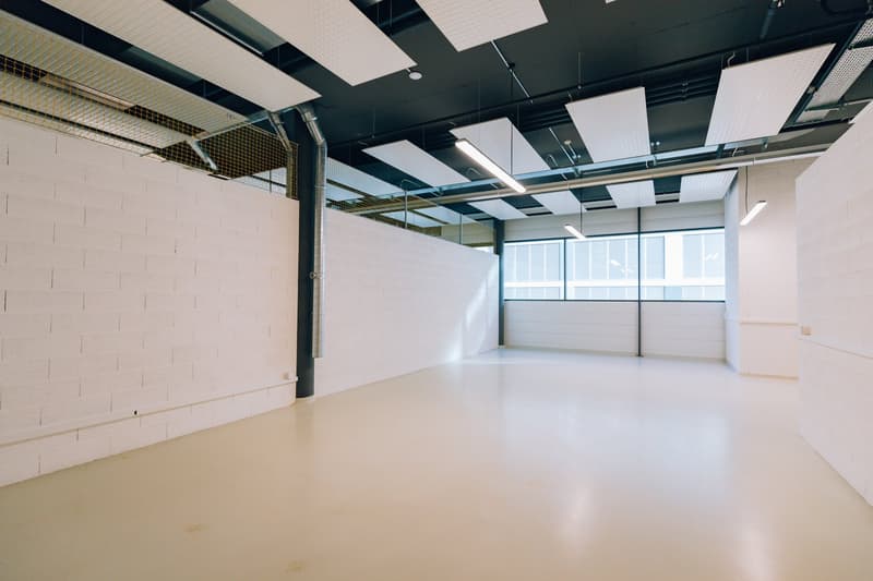open space, white walls, white floor, suspended ceiling with panels and fluorescent lights, central column