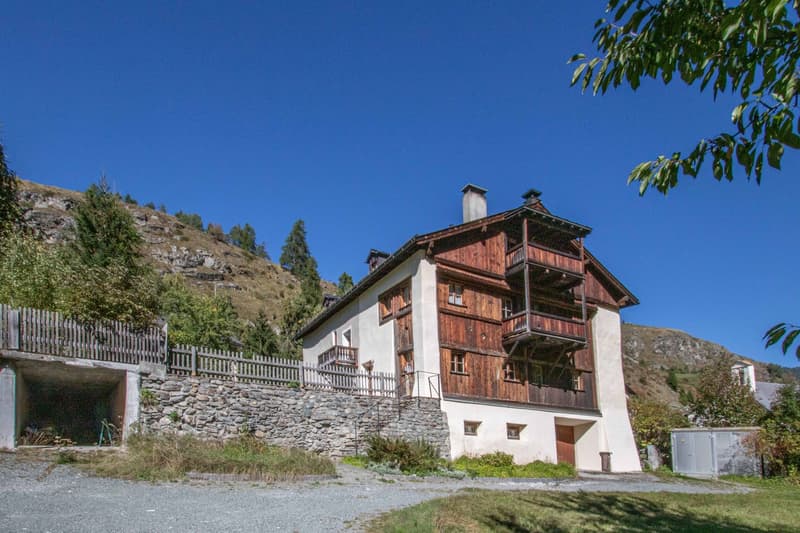 raised ground floor house, wooden exterior, balcony, garage, stone wall, mountain view
