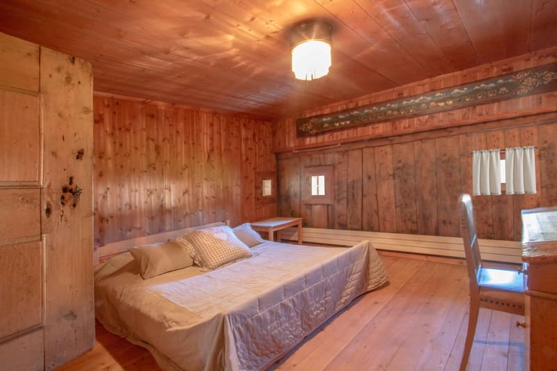 Master bedroom with bed, wooden walls and floors, window, nightstand, and chair.