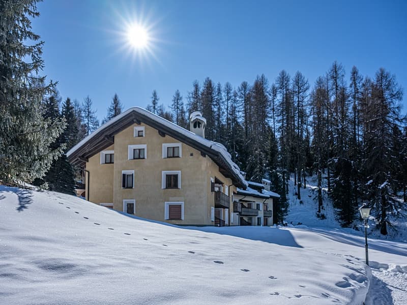 2-story house, beige exterior, covered in snow, balconies, pine trees in the background