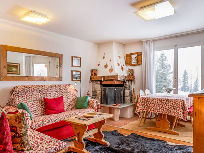 A living room with a fireplace, sofa, wooden coffee table, dining table with chairs, carpet, and framed pictures.