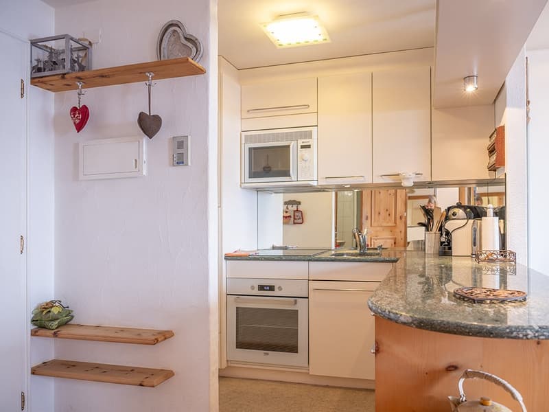 white cabinets, white countertops, integrated oven, built-in microwave, granite countertops, wooden shelves, white walls, sink, faucet, decorative items