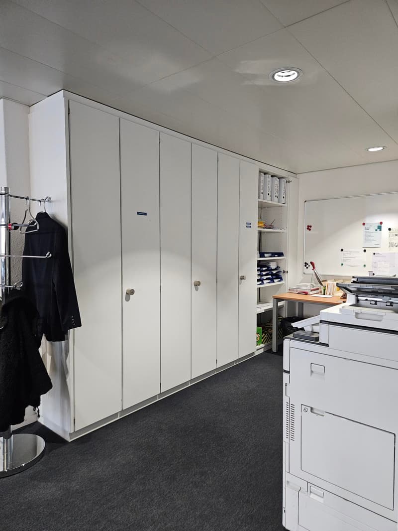 Office room with white cabinets, desk, printer, whiteboard, and clothes hanging on a rack