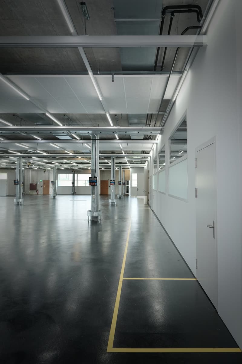 Empty large room, yellow lines marking paths, white walls, concrete floor, gray ceiling, industrial lights