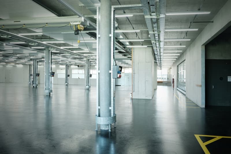 Industrial warehouse with exposed ceiling beams and overhead electrical lines, metal pillars and concrete flooring, industrial interior with gray walls