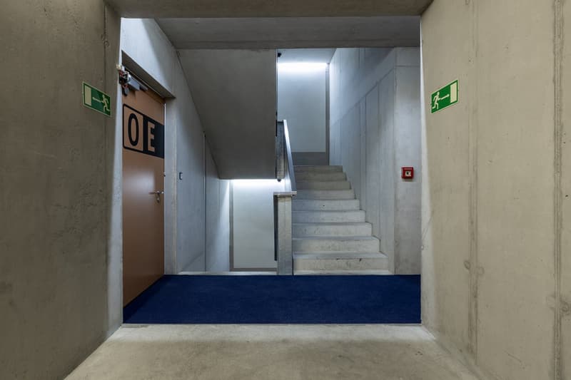 Concrete walls, blue carpet, brown door, staircase, safety sign