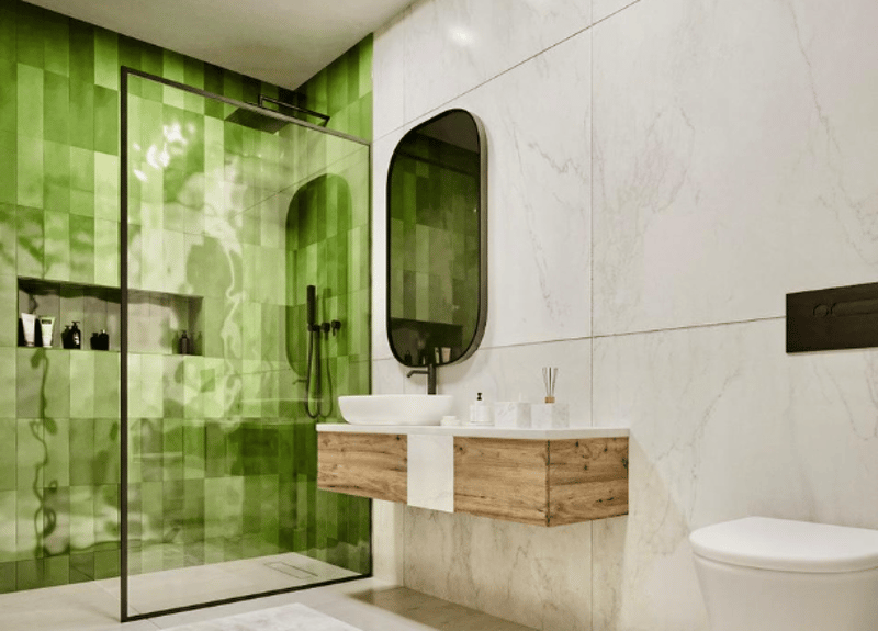 modern bathroom with green tiled walls, glass shower enclosure, wooden sink, white marble flooring, white toilet