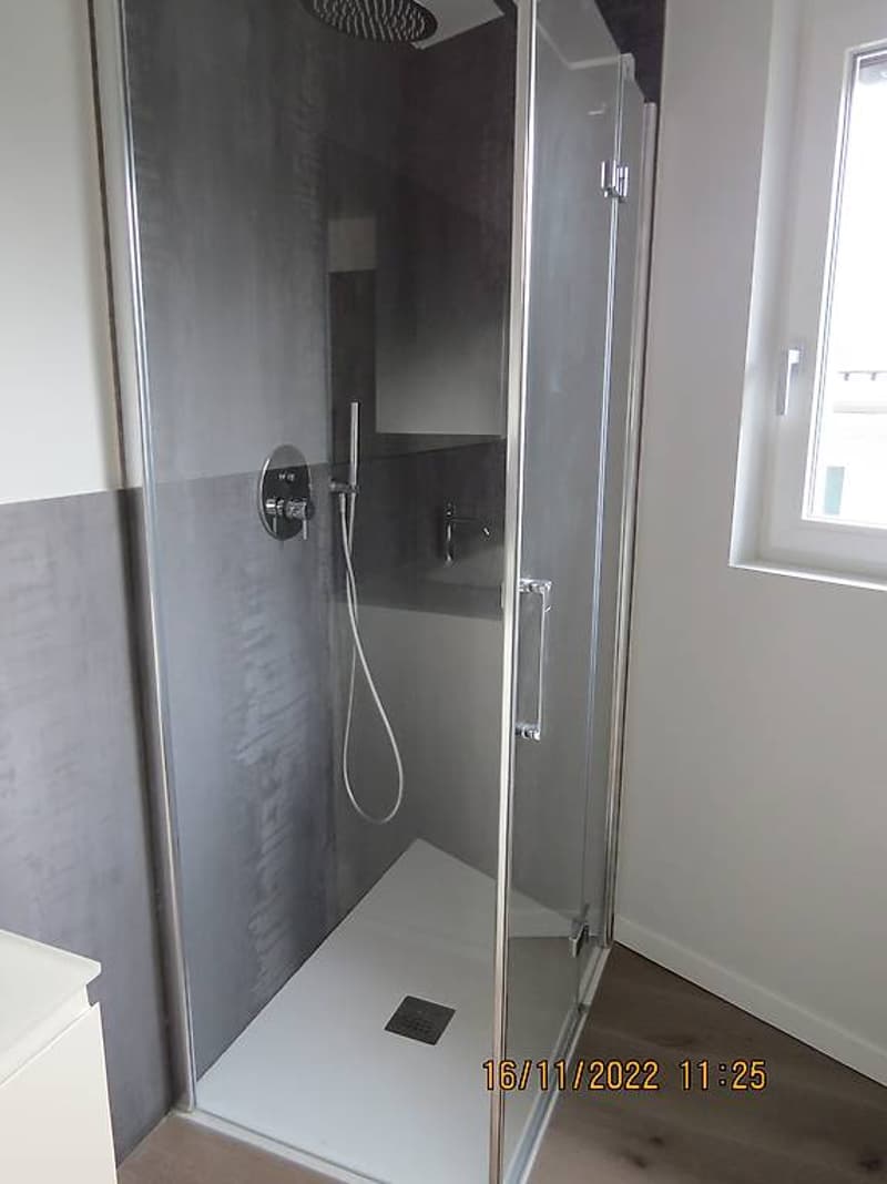 Modern walk-in shower with tiled floor, clear glass enclosure, overhead shower head and faucet