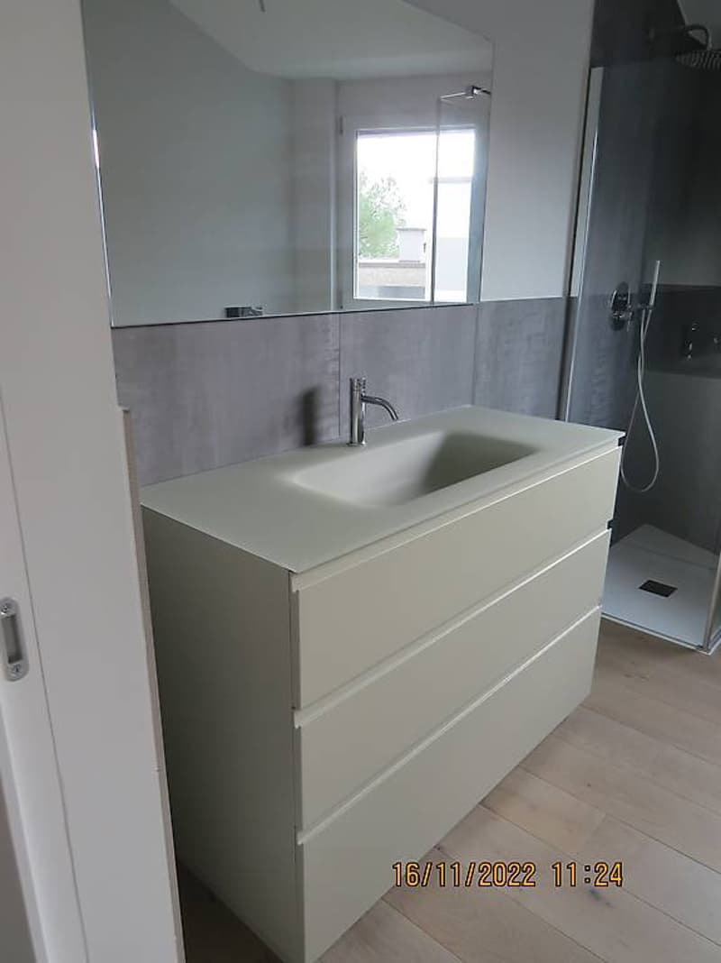 Bathroom: sink, shower, mirror, storage drawers, gray walls, wooden floor