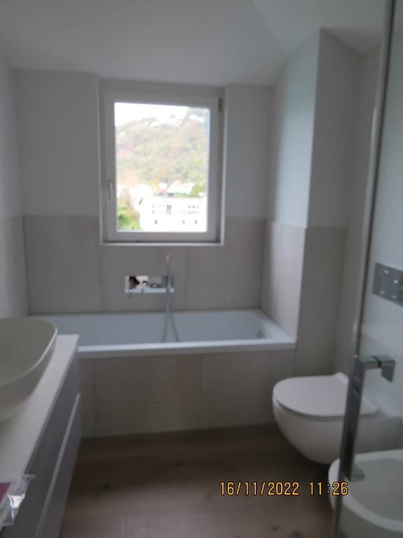 Bathroom: white bathtub, white sink, white toilet, window, tiled floor, wooden floor