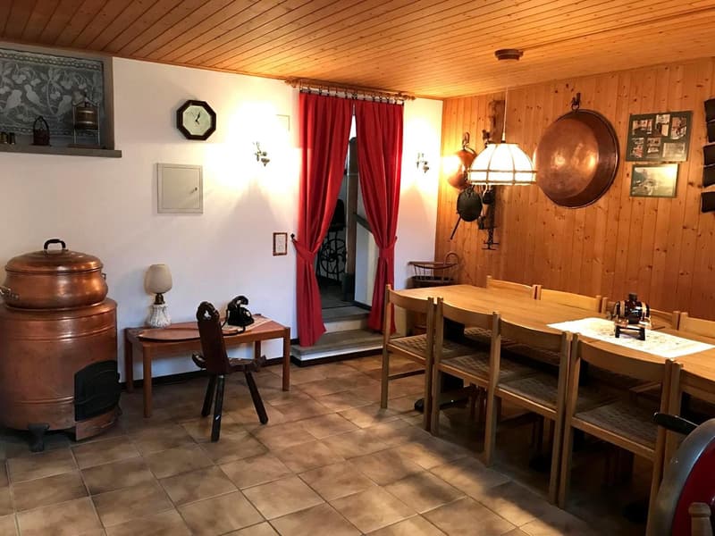 a large dining area with wooden dining table and chairs, kitchen cabinet with a lamp, red curtains at the entrance, a stove and copper utensils