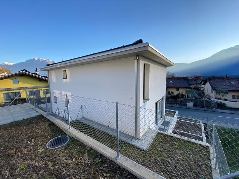 Single-story house with raised ground floor, white exterior, metal fencing, and nearby mountain views