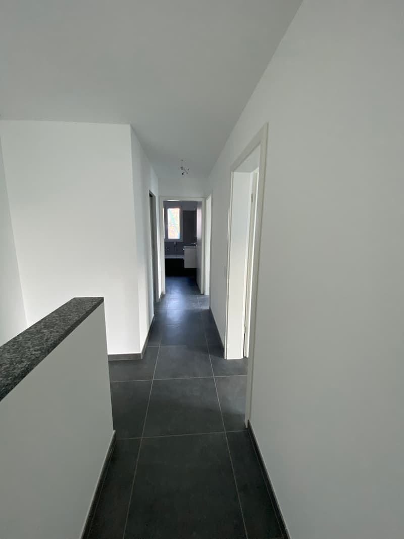 Clean and modern hallway, tiled floor, white walls, three doors, bathroom visible through one door