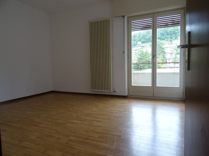 empty room with wooden floor, white walls, a window with double doors leading to a balcony, a white radiator, and a door