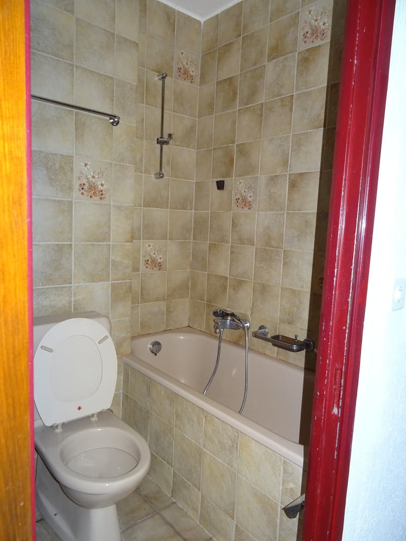 Bathroom with tiled walls and floor, bathtub with showerhead, and a toilet.