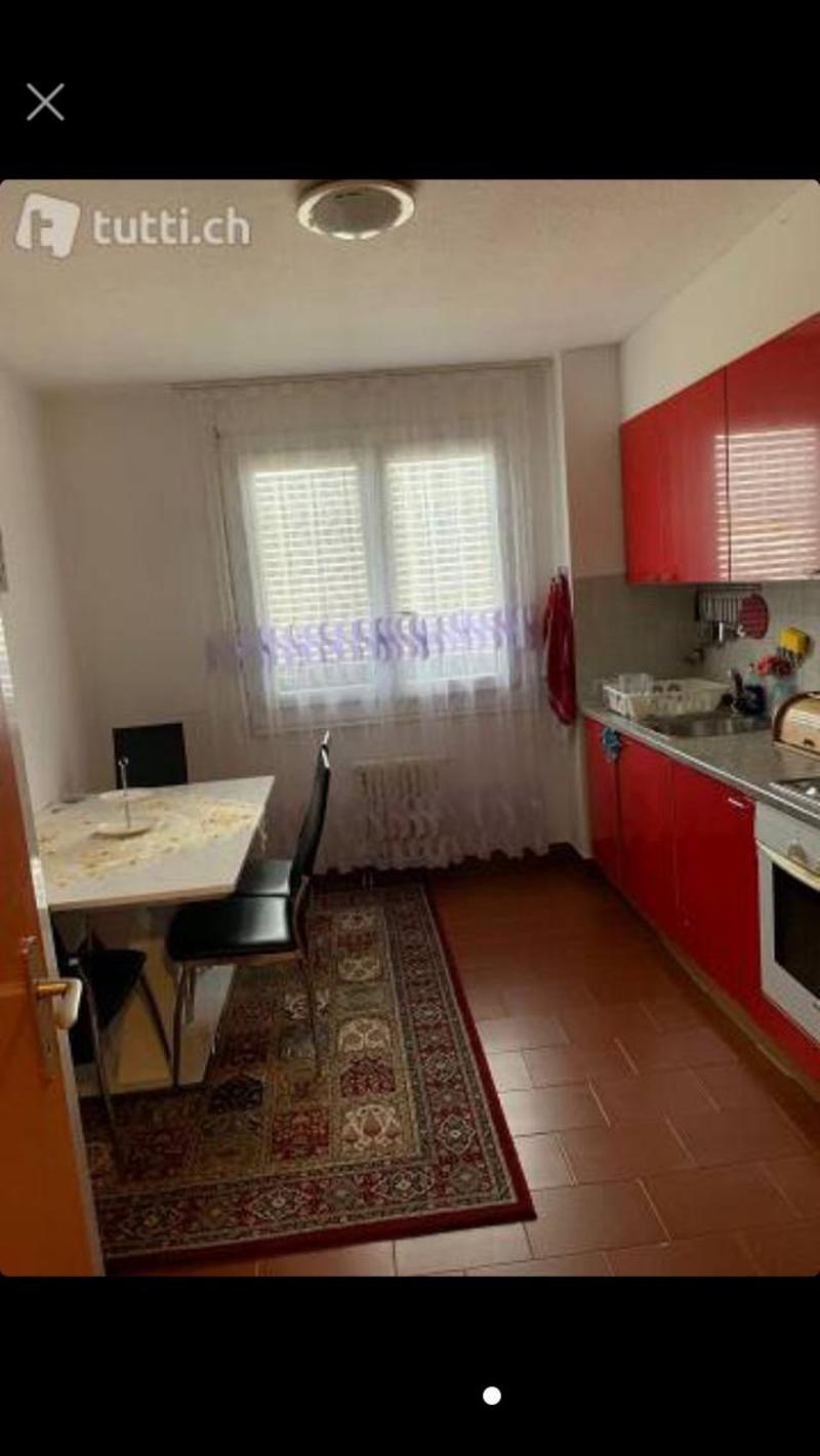 red cabinets, white tiled floor, white table with chairs, white curtains, countertop with sink and stove