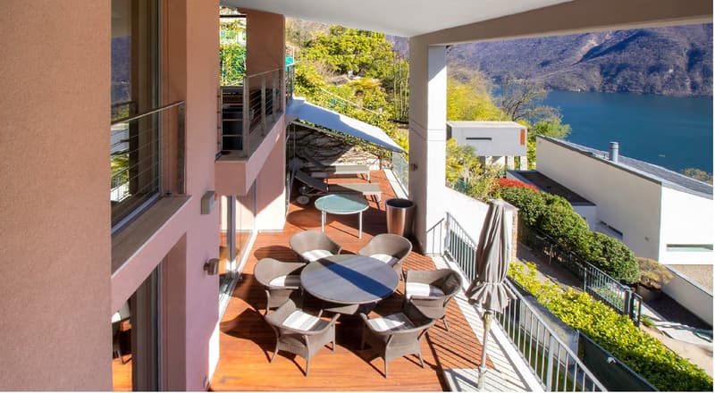 balcony with table and chairs, wooden floor, metal railings, lake view, trees, mountains