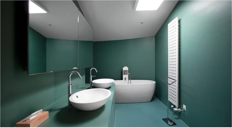Modern bathroom with green walls, two round sinks, one with a faucet, a large bathtub, a large mirror, and a white radiator.